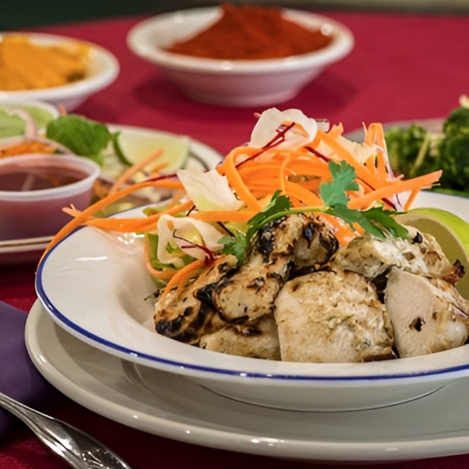 Grilled chicken pieces with shredded carrots, cabbage, and cilantro, served with lime and sauce.