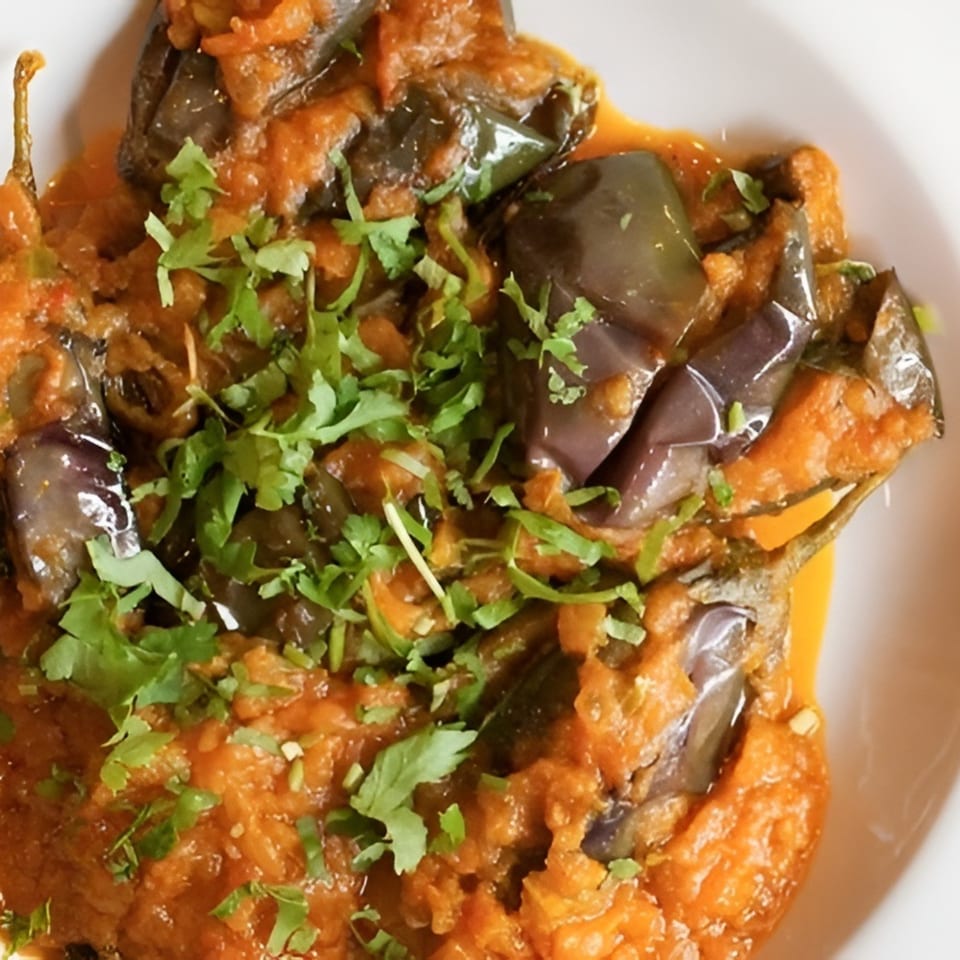 Indian Kitchen's eggplant curry, garnished with fresh cilantro, served in a white bowl.