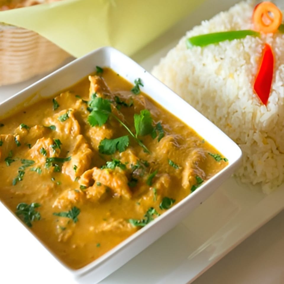 Indian chicken curry with cilantro in a white bowl, served with white rice garnished with peppers.