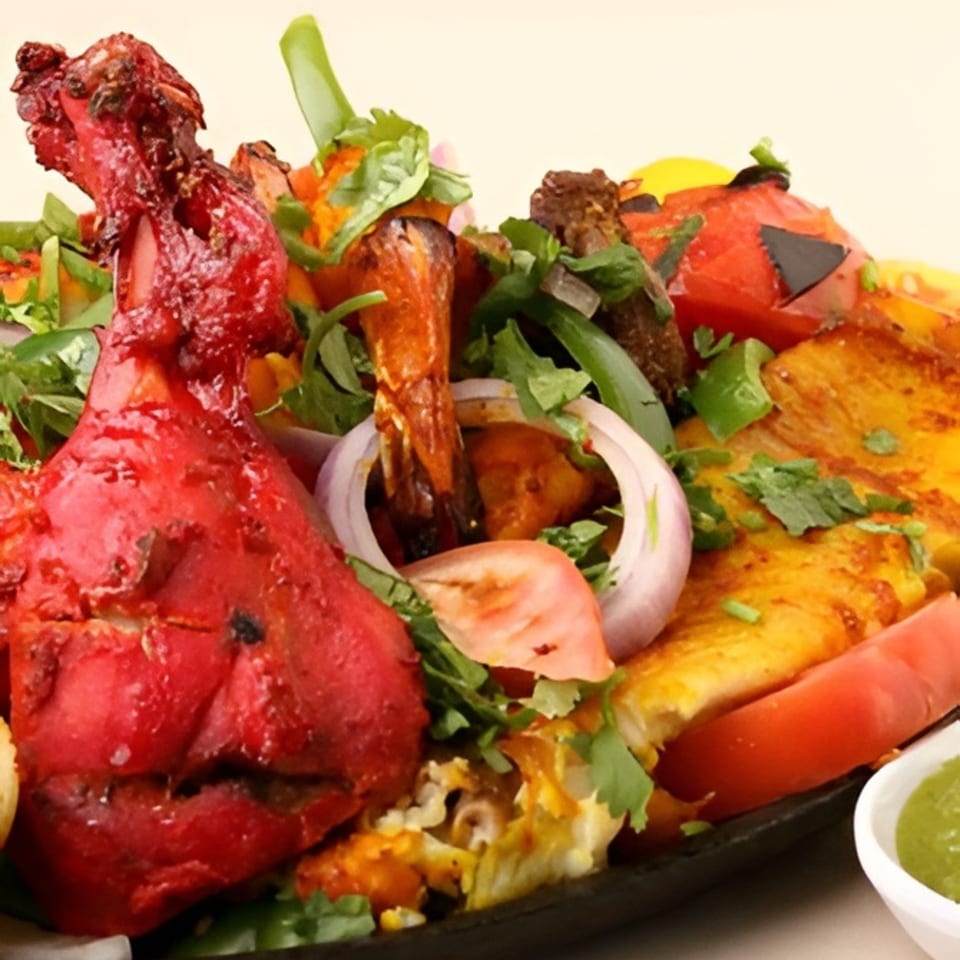 A vibrant Indian platter with tandoori chicken, shrimp, paneer, and vegetables, garnished with cilantro.