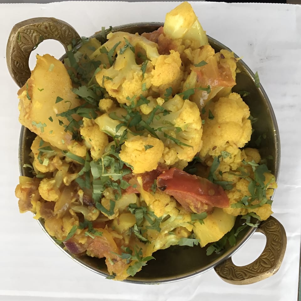 Aloo Gobi, an Indian dish with cauliflower, potatoes, and tomatoes, garnished with cilantro in a metal bowl.